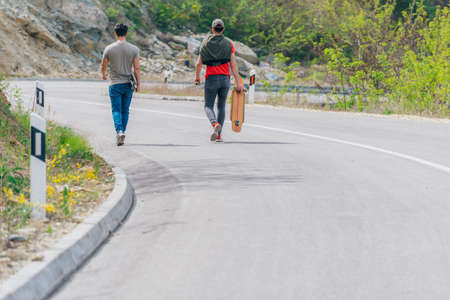 Two longboarders holding their longboards and walking downhill while chatting with eachother.の写真素材