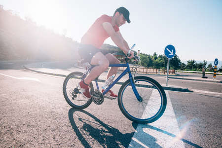Fit male biker cyclist riding his bike cycle on an asphalt road at sunset while the sun sets through his wheel.の写真素材
