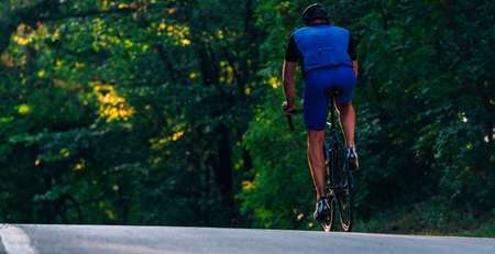Professional marathon cyclist wearing all of his safety gear rides his bike in the green nature.の写真素材