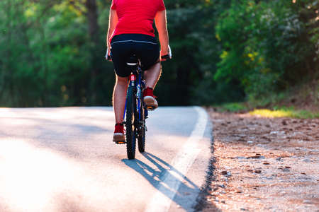 Male cyclist riding his bike on sunset on a road through deep woods. Extreme biker no safety...