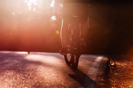 Male cyclist riding his bike on sunset on a road through deep woods. Extreme biker no safety equipment.の写真素材