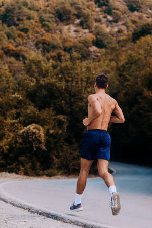 Shirtless male runner at sprinting speed training for marathon outdoors in amazing landscape. Strong and fit caucasian male fitness modelの写真素材
