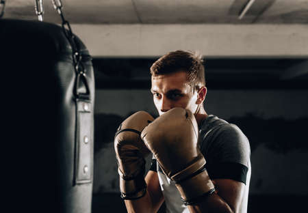 Adult boxer in boxing gloves training with boxing punching bag in a gymの写真素材