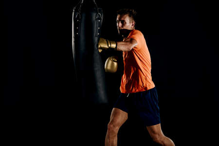 Muscular young man in boxing gloves and shorts shows the different movements and strikes on a dark backgroundの写真素材