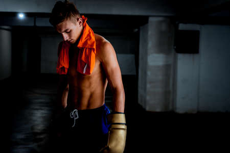 Resting time. Man with gloves and towel. Photo of sporty muscular man on dark background