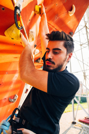 Man wearing belaying rope, climbing on a very high rock climbing wallの写真素材