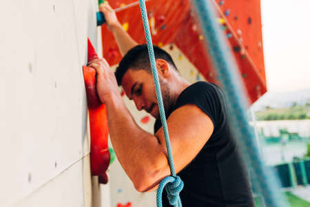 Man wearing belaying rope, climbing on a very high rock climbing wall