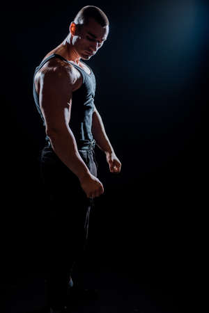 Portrait of young muscular man is flexing his muscles on dark backgroundの写真素材