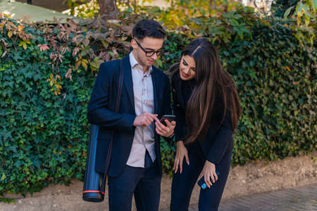 Young attractive businesswoman talking on the phone while standing outside with her male colleague
