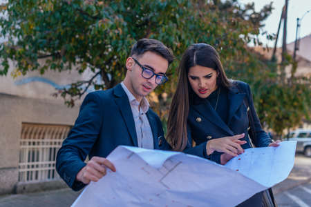Business male and female architects looking at the blueprint about a building project outdoors.