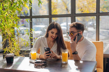 Friends socializing, having fun, and laughing drinking coffee in coffeehouse while fooling around. Male and female friends Taking pictures together on a sunny day.の写真素材