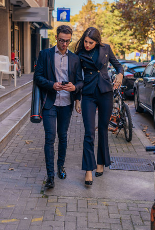 Business man and woman holding mobile phone and talking standing on the streets