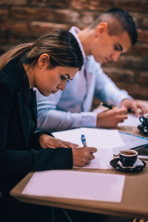 Young couple signing paper contract together at business meeting in a cafe bar