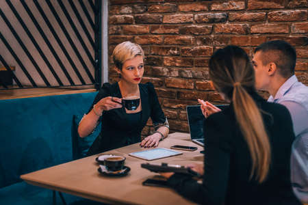 Young blonde female consultant drinking coffee during her business meeting in a cafeteriaの写真素材