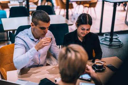 Top view of a beautiful young couple talking to their realtor while using tablet and drinking coffee at table in cafeの写真素材