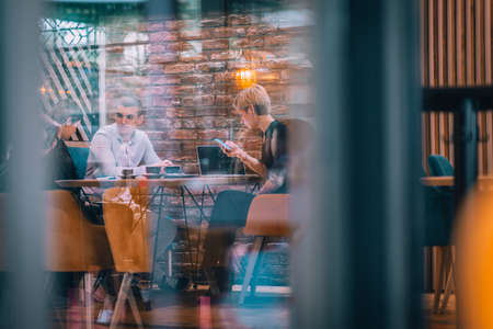 Business meeting inside a cafe with young colleagues sitting at a table, sharing some new ideas while the focus is through a cafe window.の写真素材
