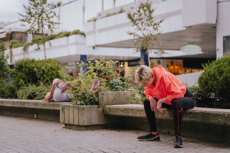 Athletic female runners sitting and resting on a bench in an urban environmentの写真素材