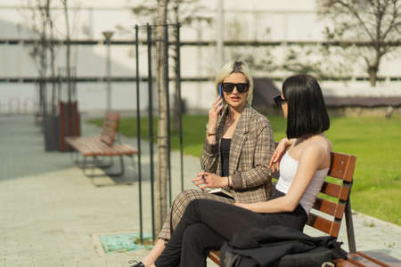 Two businesswomen are organising the meeting while only one of them is talking on the phone
