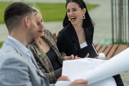 Three business people are laughing at each other while sitting on the bench