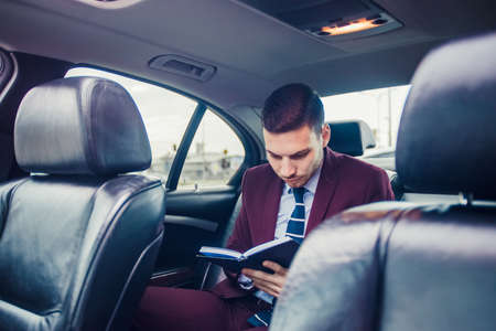 Businessman is driving in his limo and writing in his notebookの写真素材