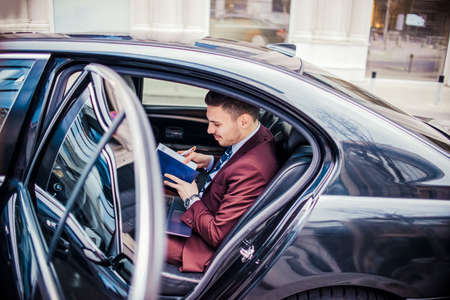 Man in purple suit looking in his notebook while sitting in automobileの写真素材