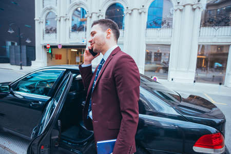 Entrepreneur Businessman standing in an urban area next to his limo while talking on the phone.の写真素材