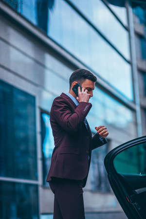 Entrepreneur(Businessman) standing in an urban area and wearing a suit and tie next to his limo while talking on the phone.の写真素材