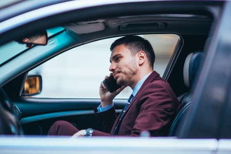 A manager sitting at the front seat of his limo talking on his cellphone while making a lot of hand gestures.の写真素材