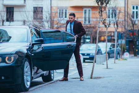 Entrepreneur(Businessman) standing in an urban area and wearing a suit and tie next to his limo while talking on the phone.の写真素材