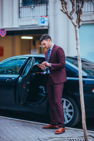 Entrepreneur(Businessman) standing in an urban area and wearing a suit and tie next to his limo while talking on the phone.の写真素材