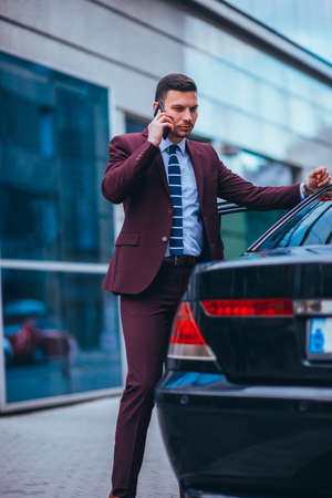 Entrepreneur(Businessman) standing in an urban area and wearing a suit and tie next to his limo while talking on the phone.の写真素材