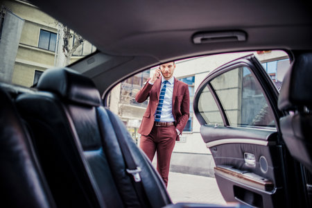 Young businessman is outside and talking on mobile near the limousineの写真素材