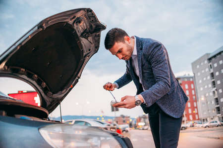 Young manager formally dressed checking his car oil at sunset while leaning under the car's hood.の写真素材