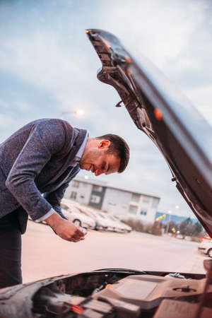 Young manager formally dressed checking his car oil at sunset while leaning under the car's hood.の写真素材