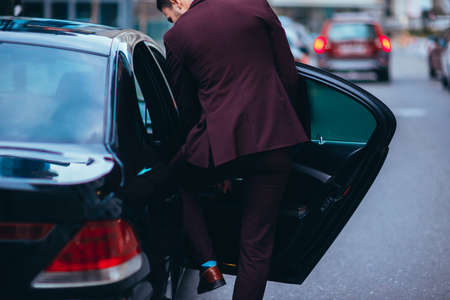 Handsome suited businessman entering the back of his black limo.の写真素材