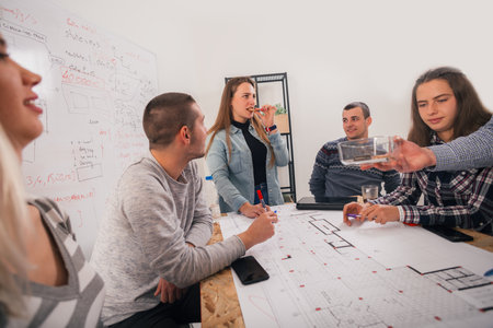 A group of young entrepreneurs discussing their next project at a meeting pointing at the blueprint...
