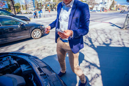 A businessman has parked his car at the side of the boulevard while he checks his car oil, on a...