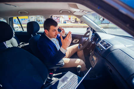 Reckless businessman driving in the city during the rush hour while typing on his laptop and acting...