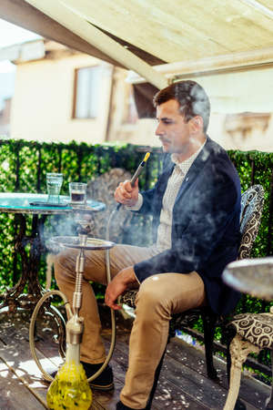Attractive man on terrace enjoying in the sun while smoke shishaの写真素材