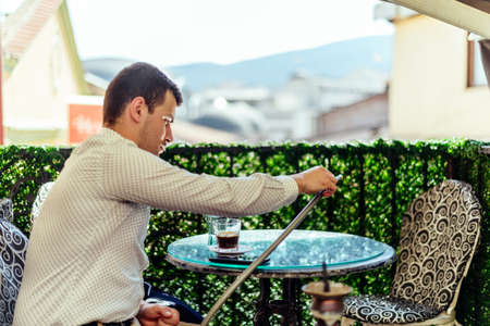 Urban young man relaxing in bar while drink coffee and smoking hookah
