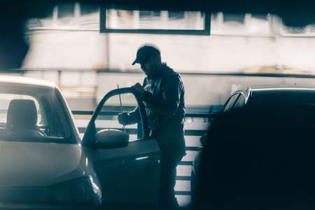 Young masked thief is robbing a car