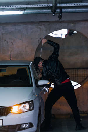 Dangerous man is standing next to a car and trying to rob it