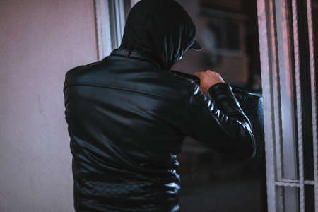Robbery man wearing hoody try to break into the house with wrecking barの写真素材