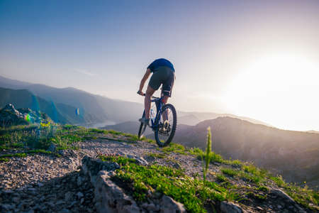 Adventurous Cyclist riding his mountain bike at the edge of a cliff, on rocky terrain while wearing no safety equipment.Amazing top view.の写真素材