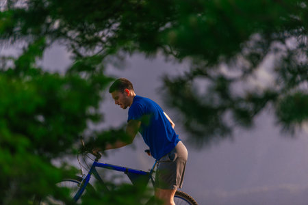 Tired cyclist is wiping his sweat off his face while pushing his bicycle uphill on a dirt road in a mountain.の写真素材