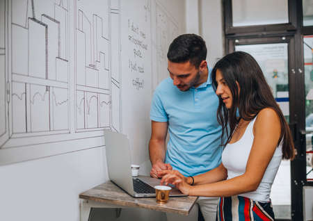 Handsome man using pc lap top in a coffee shop with his female partner, near the coffee cups