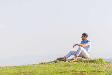 Well dressed ( fashionable) man stands in nature looking over a cliff at the large lake and mountain line while wearing boat shoes, polo shirt and formal pants.の写真素材