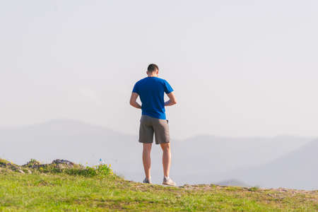 A fit male athlete is preparing for a work out in nature while looking over a cliff at the large lake and mountain line.の写真素材