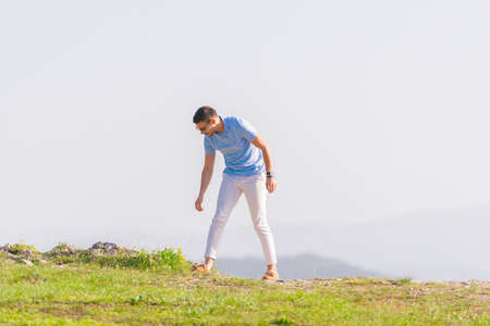 Well dressed ( fashionable) man stands in nature looking over a cliff at the large lake and mountain line while wearing boat shoes, polo shirt and formal pants.の写真素材