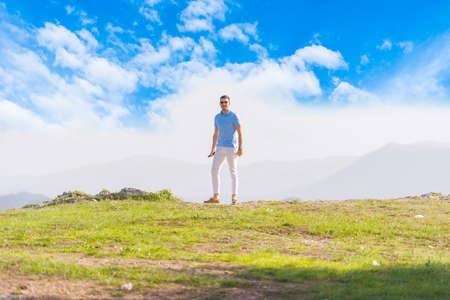 Well dressed ( fashionable) man stands in nature looking over a cliff at the large lake and mountain...